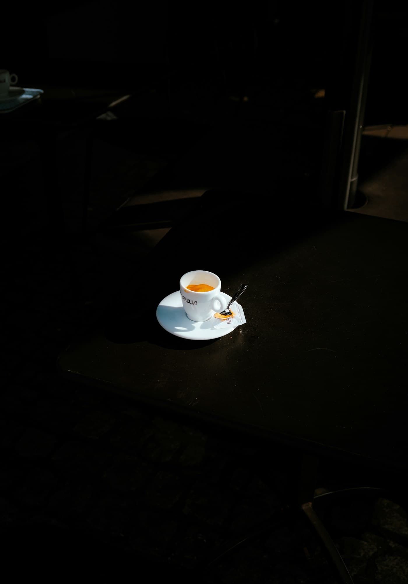 A single espresso and its saucer on a dark table, caught in a narrow shaft of light.